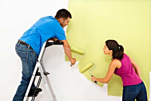 Attractive young adult couple painting interior wall of house.